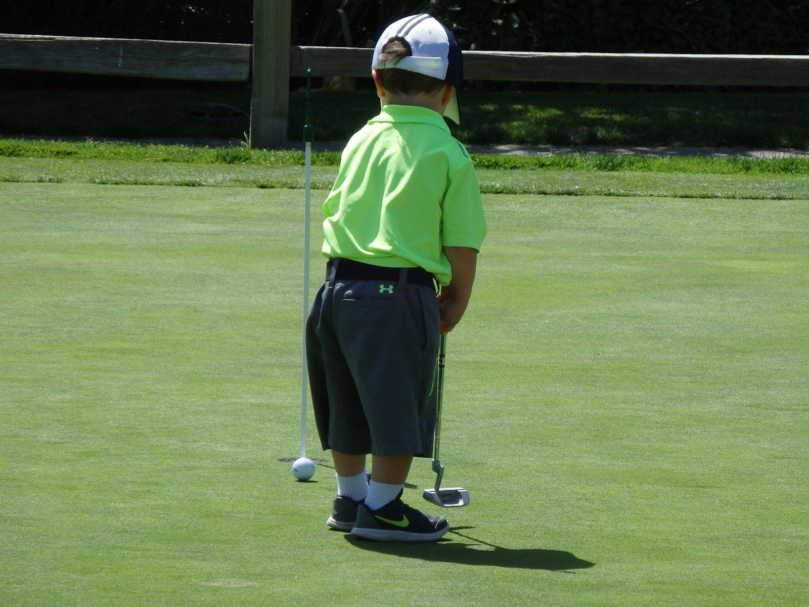 Jeune enfant vu de dos, un putter à la main, sur un green de golf