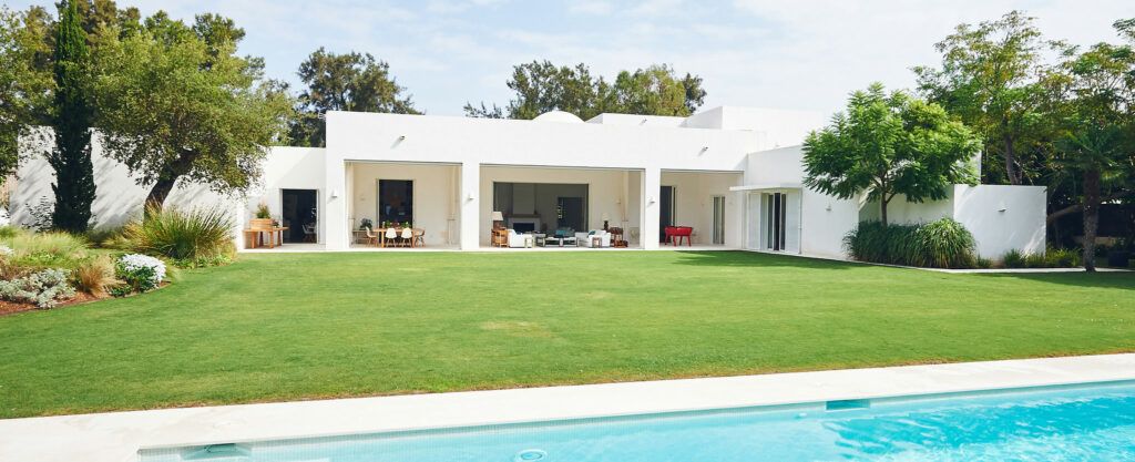 Façade blanche de la villa, pelouse et piscine, à Sotogrande